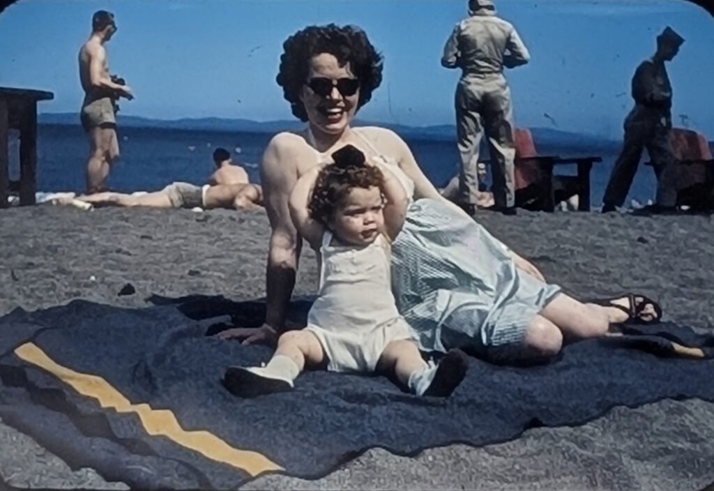 Smiling woman on a beach with toddler on beach blanket